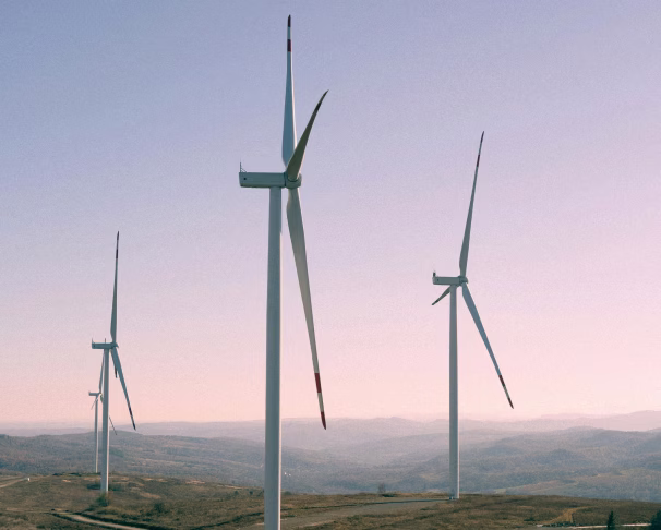 Three wind turbines on a hill with distant mountains under a clear sky at sunset.