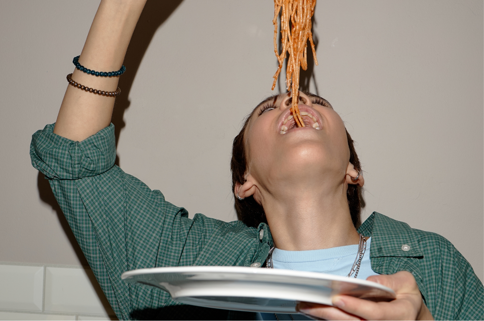 Person tilting their head back to catch a forkful of spaghetti, holding an empty plate underneath