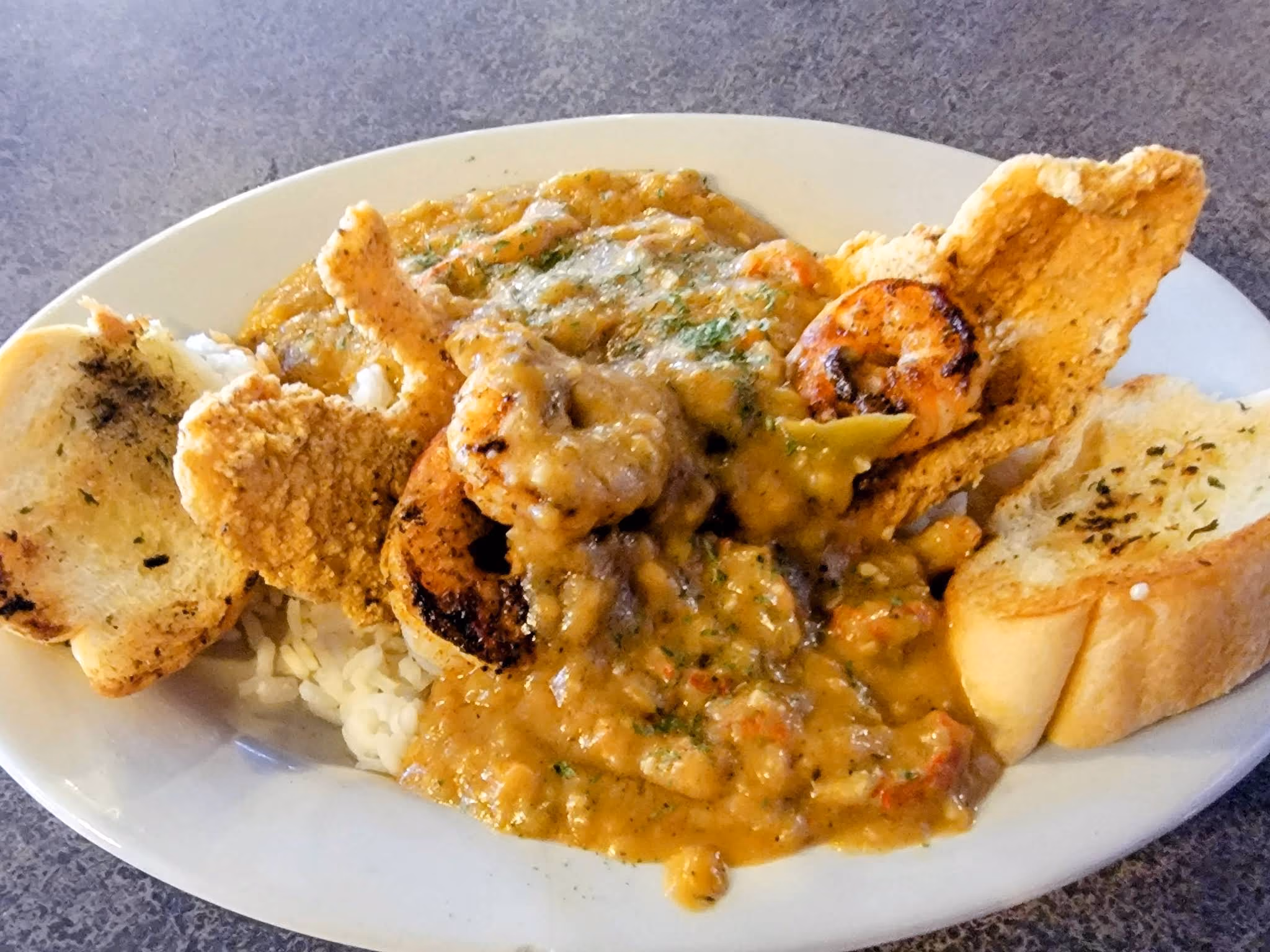 Plate of shrimp and grits with sauce, grilled shrimp, fried pork rind, and two pieces of garlic bread.