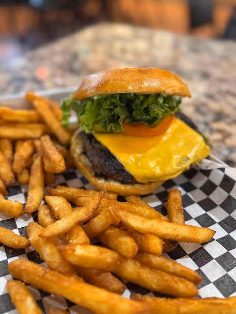 Cheeseburger with lettuce and tomato served with crispy French fries on checkered paper.