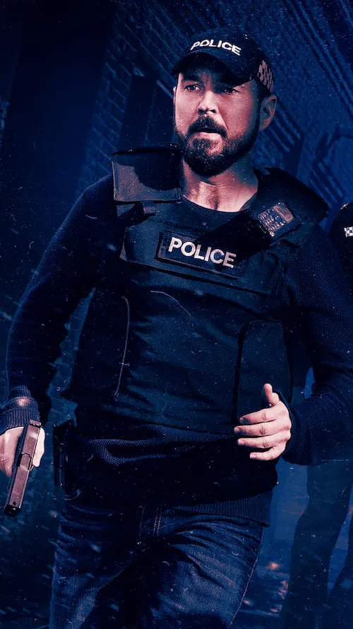 Bearded police officer in black tactical gear and cap marked 'POLICE' holding a handgun, running in a dimly lit urban setting.