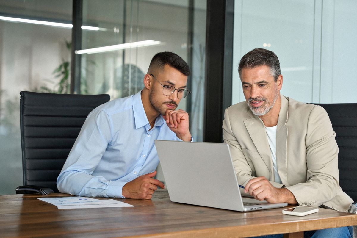 Two men looking at a laptop screen together in a conference room.