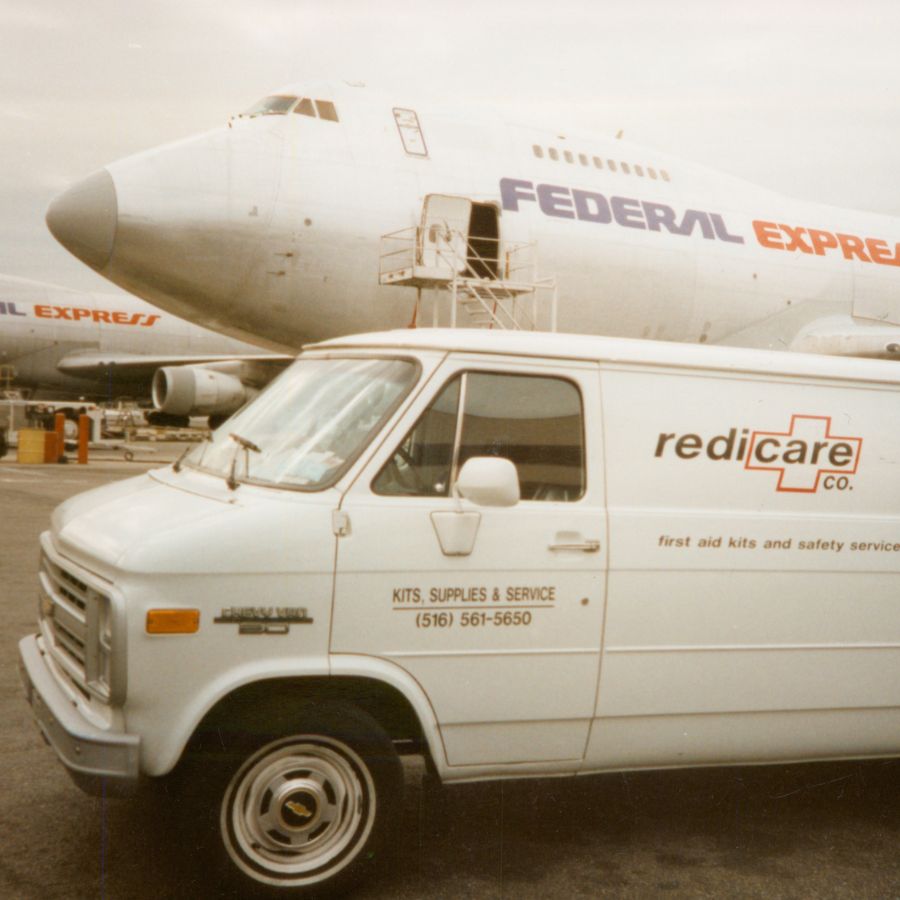 An old Redicare van parked in front of a 'Federal Express' jet on the tarmac.
