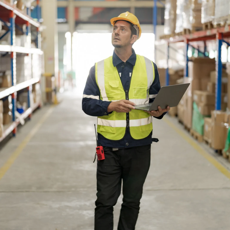 A man in safety gear holding a laptop and inspecting a facility