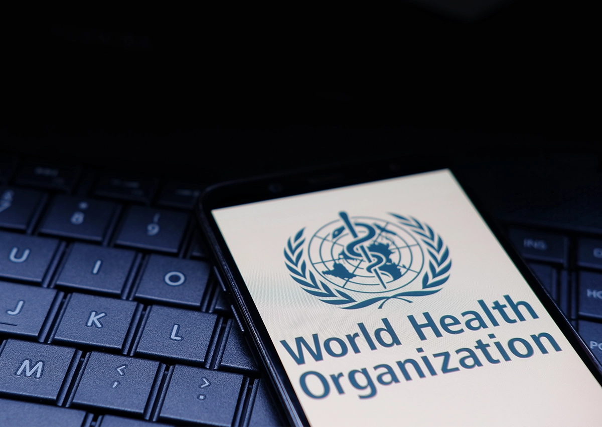 Smartphone displaying the World Health Organization logo resting on a computer keyboard.
