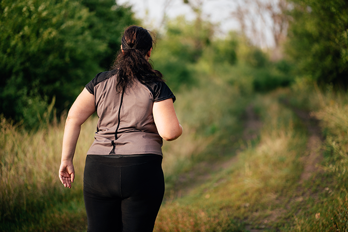 Person jogging on a dirt path surrounded by green trees and grass.