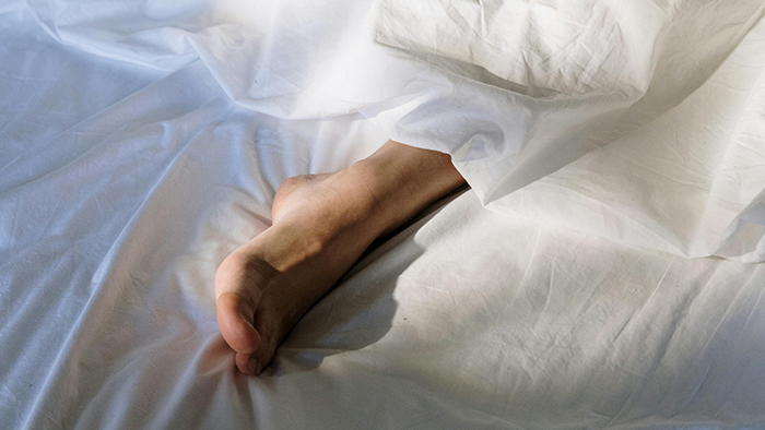 A person’s bare foot sticking out from under white bed sheets on a white bed.