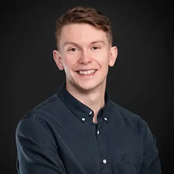 Smiling young man with short brown hair wearing a dark button-up shirt against a black background.