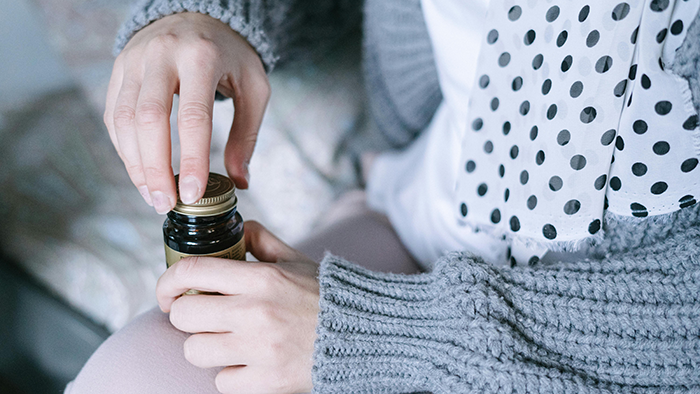 Person wearing a gray sweater and polka dot scarf opening a small brown medicine bottle.