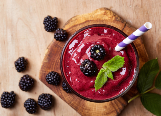 A bowl of berry smoothie topped with fresh berries and mint is placed on a table. The image illustrates smoothies as part of a balanced diet and their potential role in supporting weight loss.