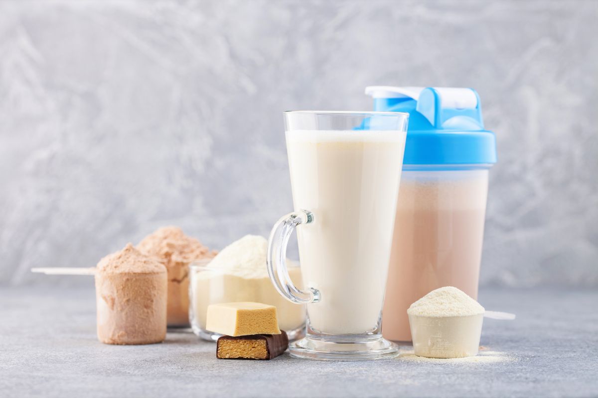 A shaker bottle, a glass of meal replacement shake and protein powder are placed on a table. The image illustrates meal replacements for weight loss and highlights their potential benefits and drawbacks as part of a weight management programme.