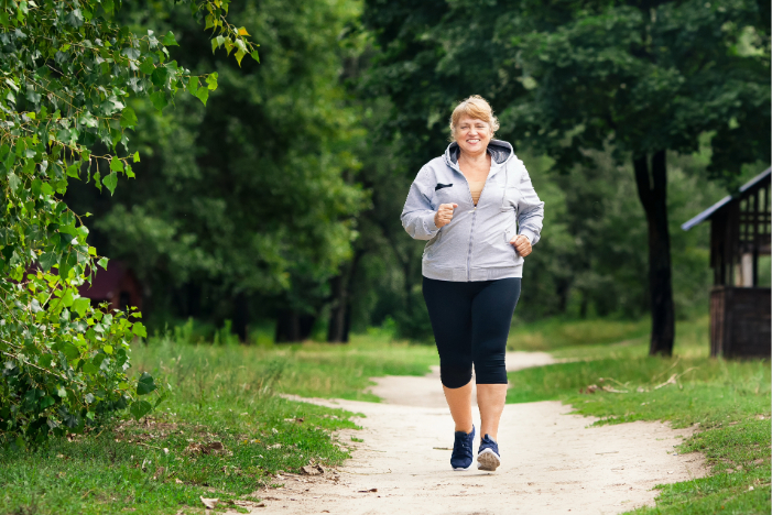 Smiling woman jogging on a dirt path in a green park with trees and grass.