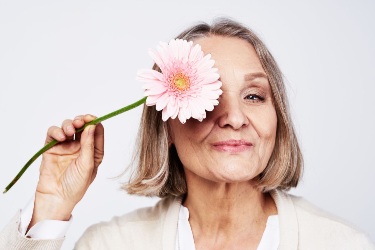 An older woman holding a flower up to one eye