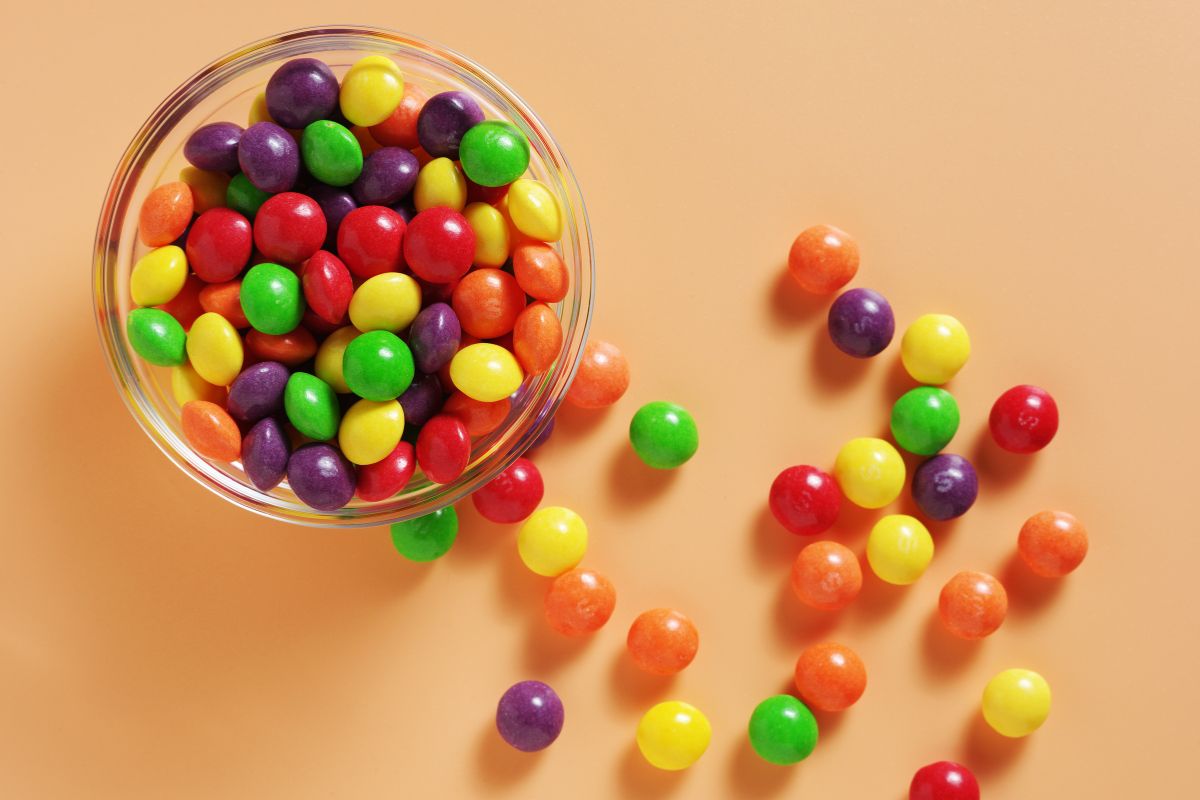 Glass bowl filled with colorful candy-coated chocolates, with some scattered on a peach-colored surface.