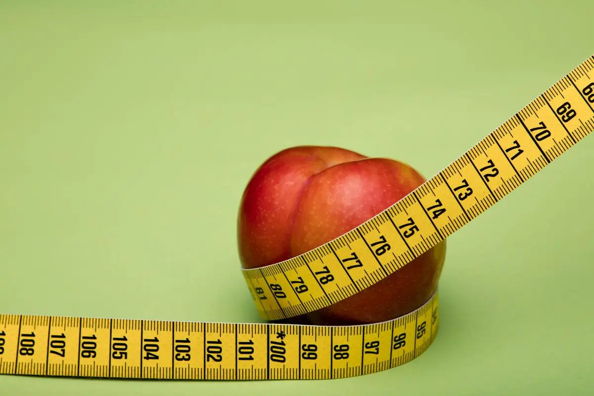 Red apple wrapped with a yellow measuring tape on a green background.