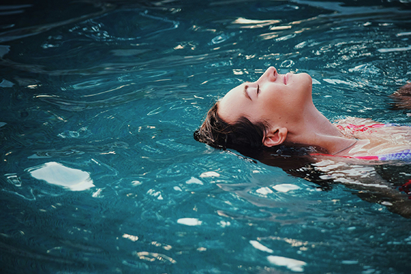 Woman floating relaxed on her back in a swimming pool with eyes closed.