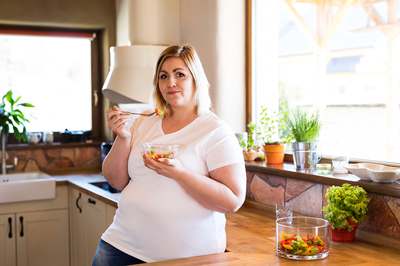 A woman standing in the kitchen, eating a salad