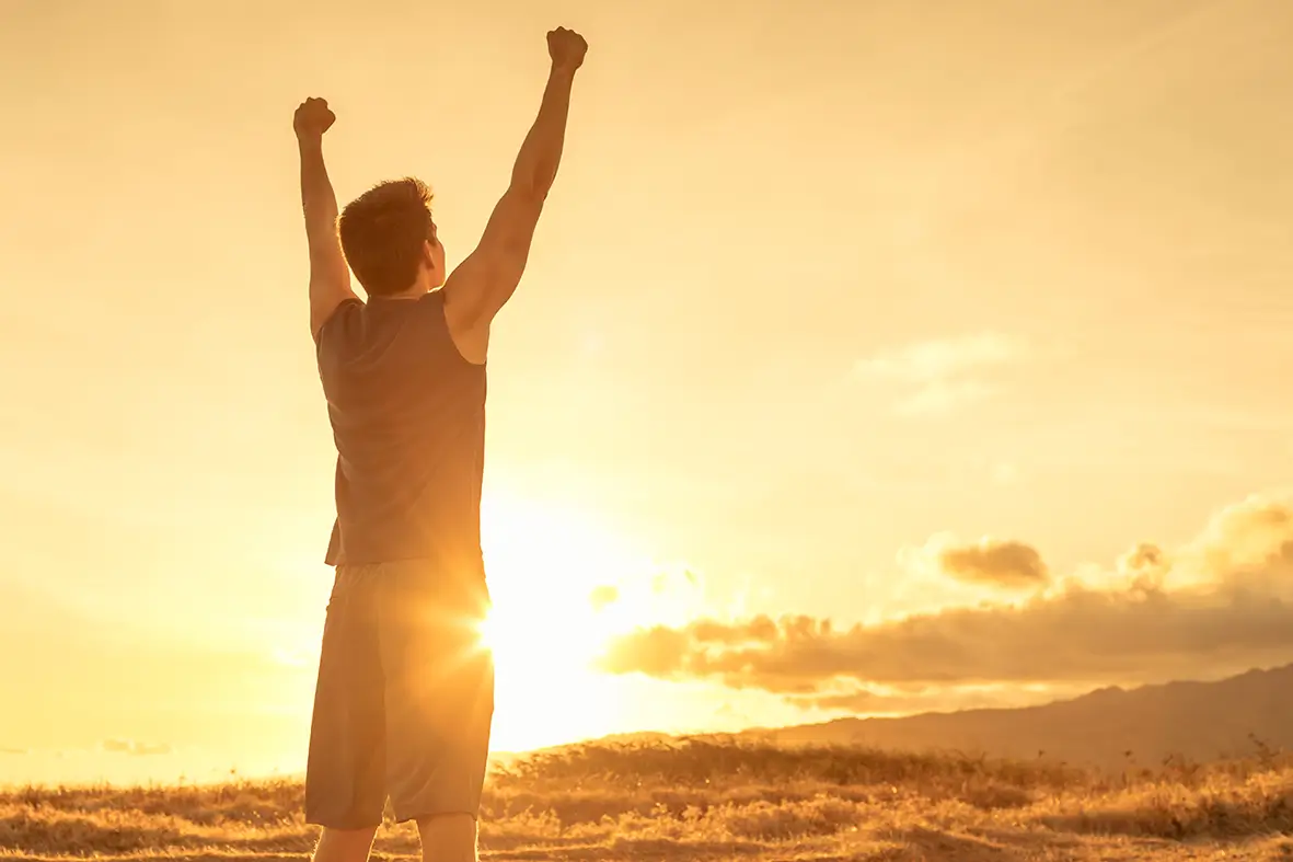 Man raising his fists in triumph while standing outdoors at sunset.
