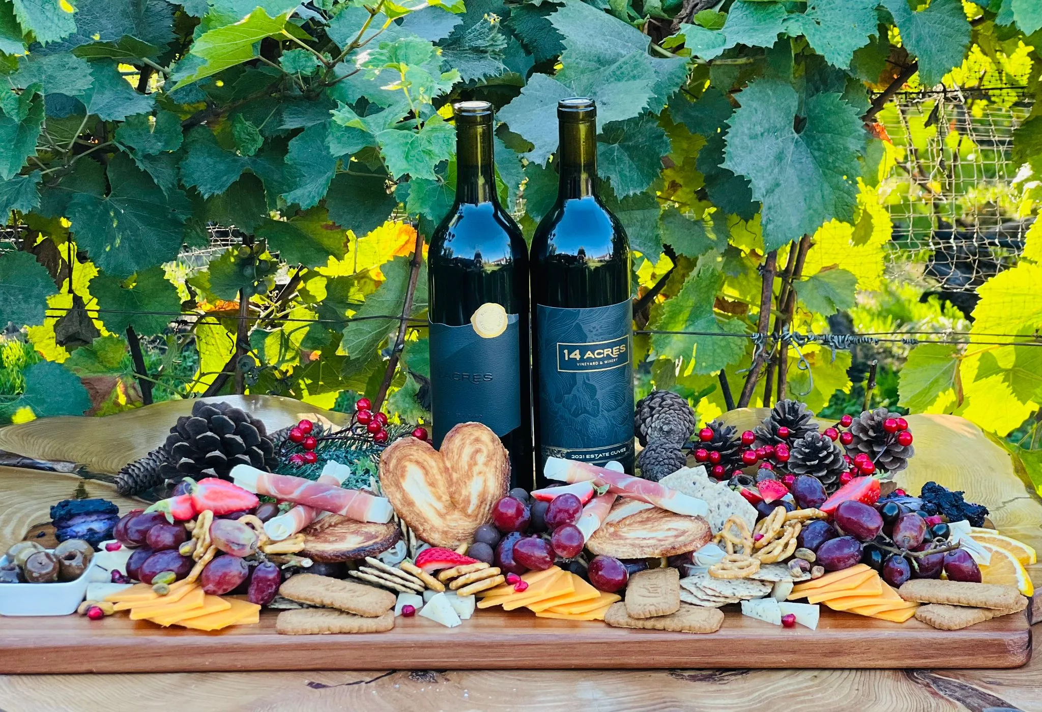 A long grazing board of meats, cheeses, crackers and fruit with two bottles of 14 Acres wine, under the grapevines