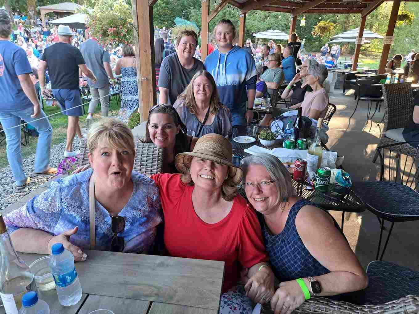 Three women smiling at a table under the covered patio during a busy event at 14 Acres