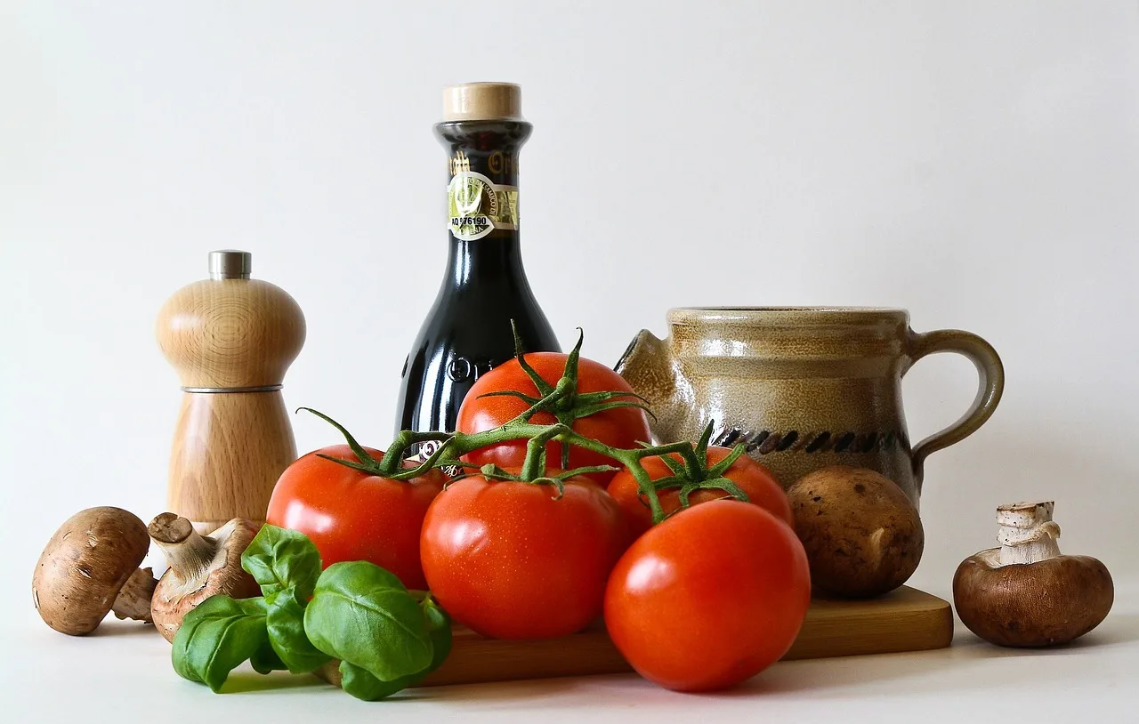 Vine tomatoes, basil, mushrooms, a pepper grinder and a stoneware jug arranged on a white background