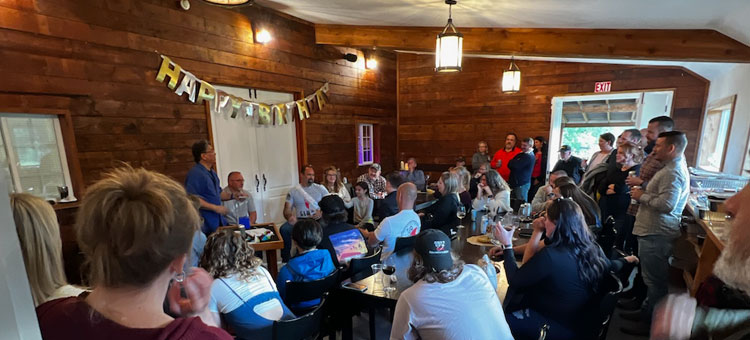 A crowded birthday party in the wood-panelled tasting room at 14 Acres under a Happy Birthday banner