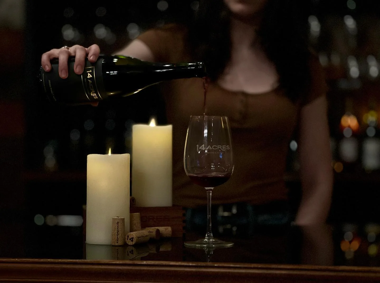 Red wine being poured into a 14 Acres glass by candlelight at the tasting bar