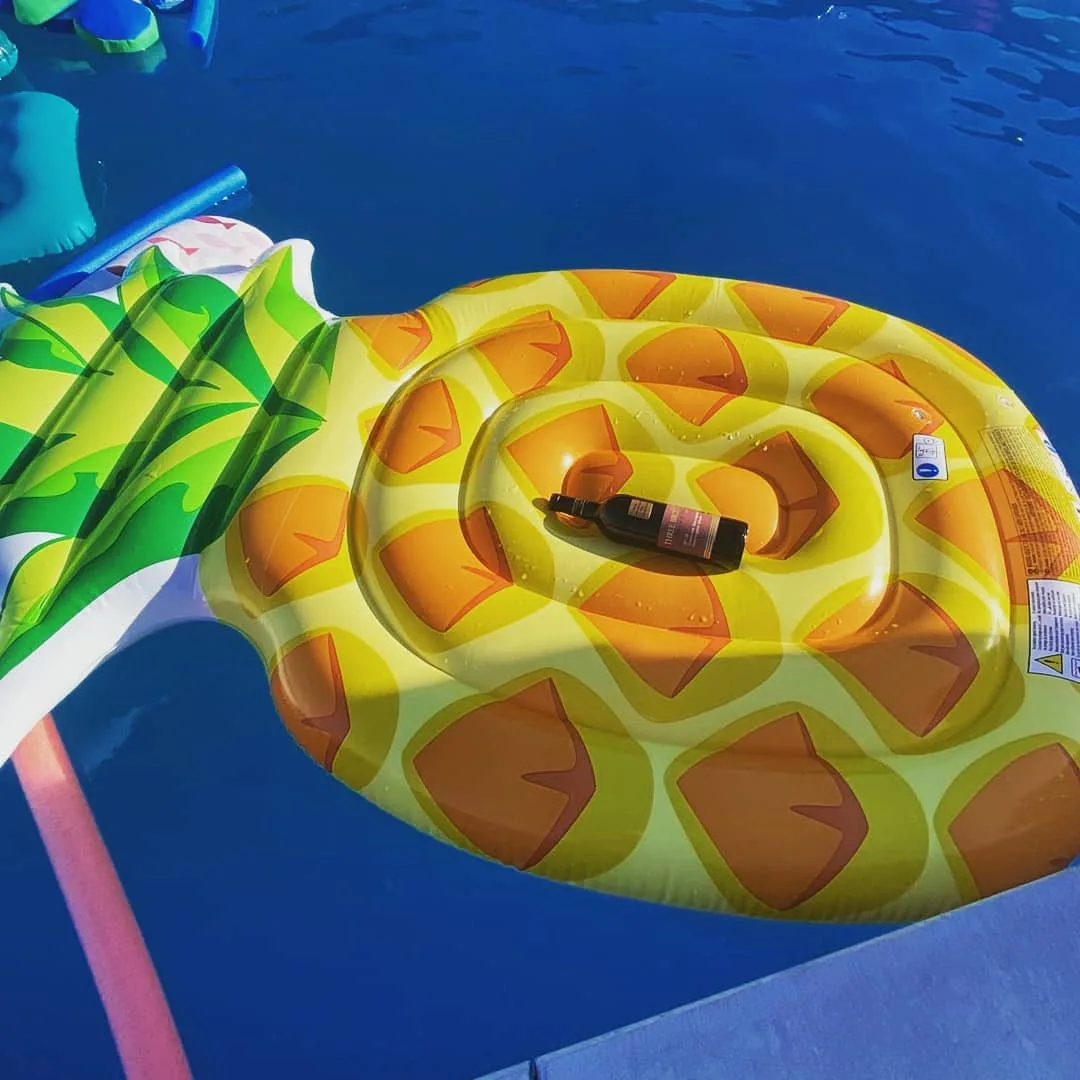 A can of wine resting on a pineapple pool float in a swimming pool