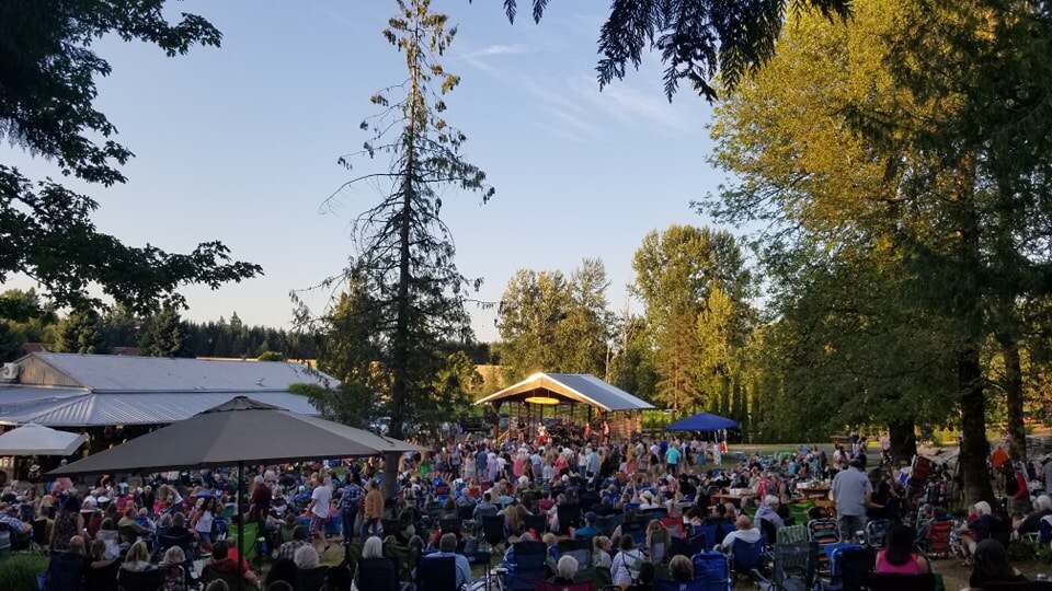 A large crowd seated on the lawn at 14 Acres for an outdoor concert at golden hour