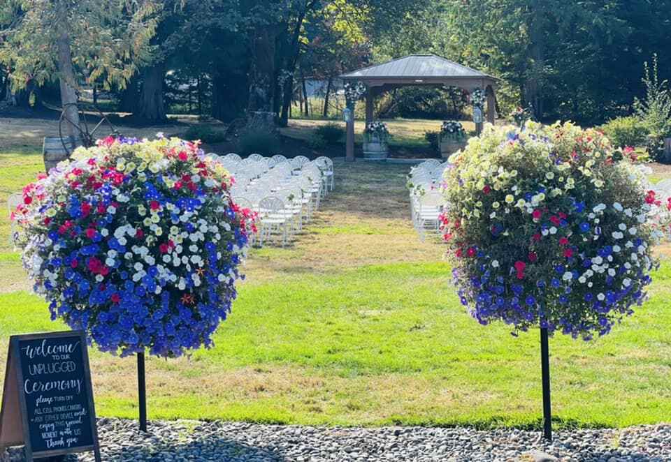 White chairs set up facing the gazebo on the lawn at 14 Acres, flanked by flowering topiaries
