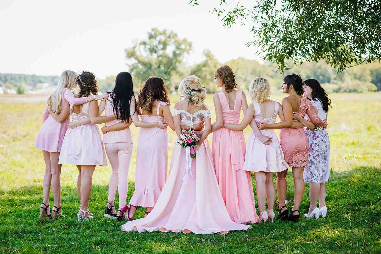 A bride and her bridesmaids in pink dresses standing arm in arm with their backs to the camera