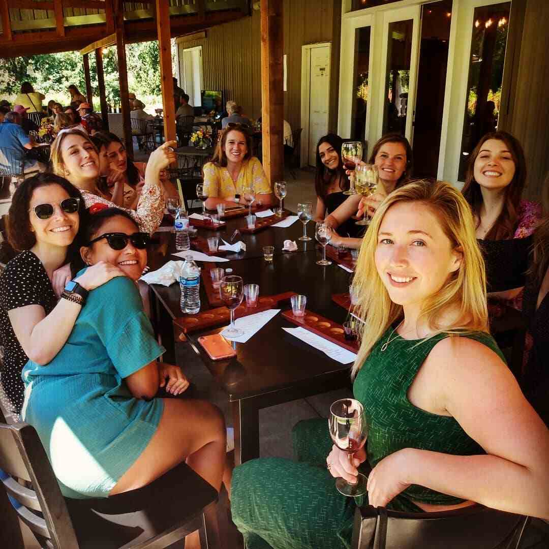 A long table of women smiling together during a party on the covered patio at 14 Acres