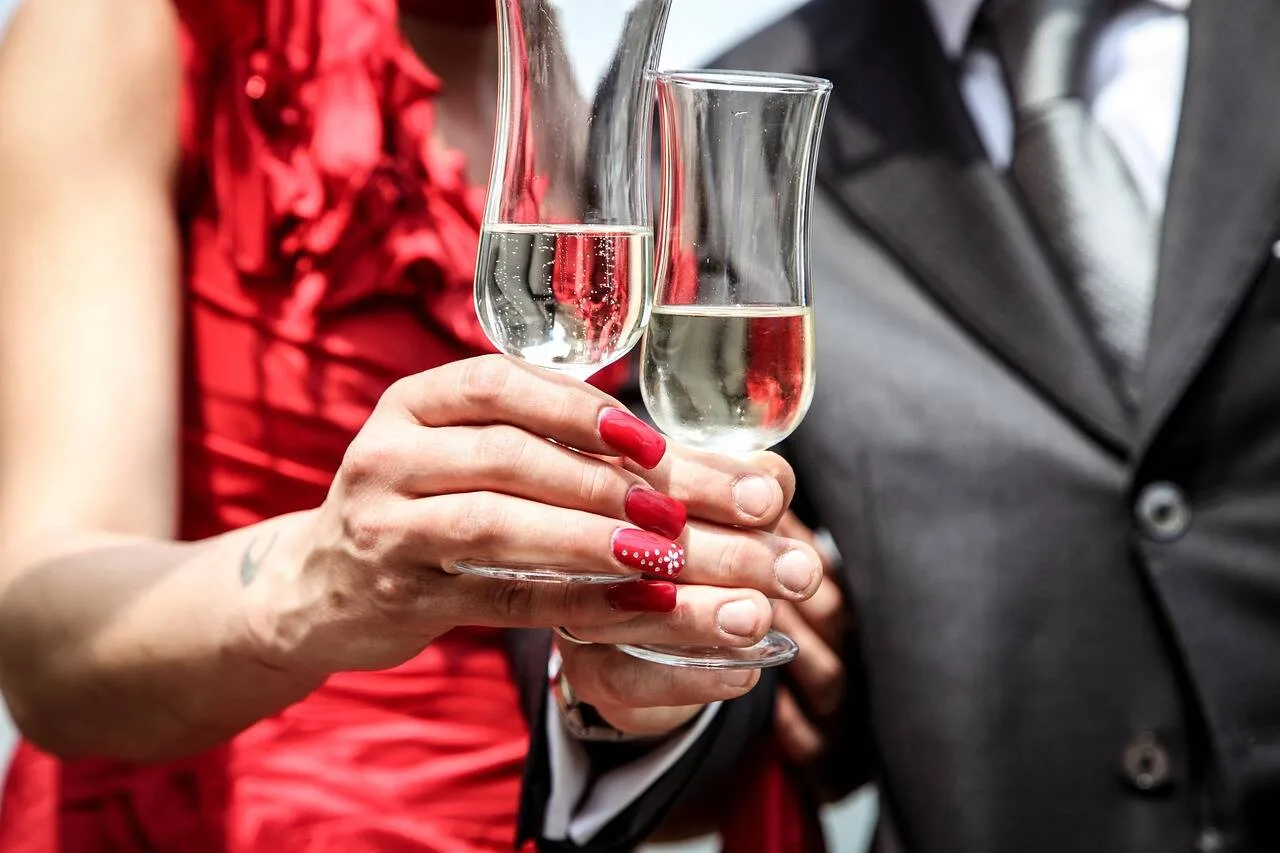 A couple in a red dress and a suit toasting with two glasses of sparkling wine