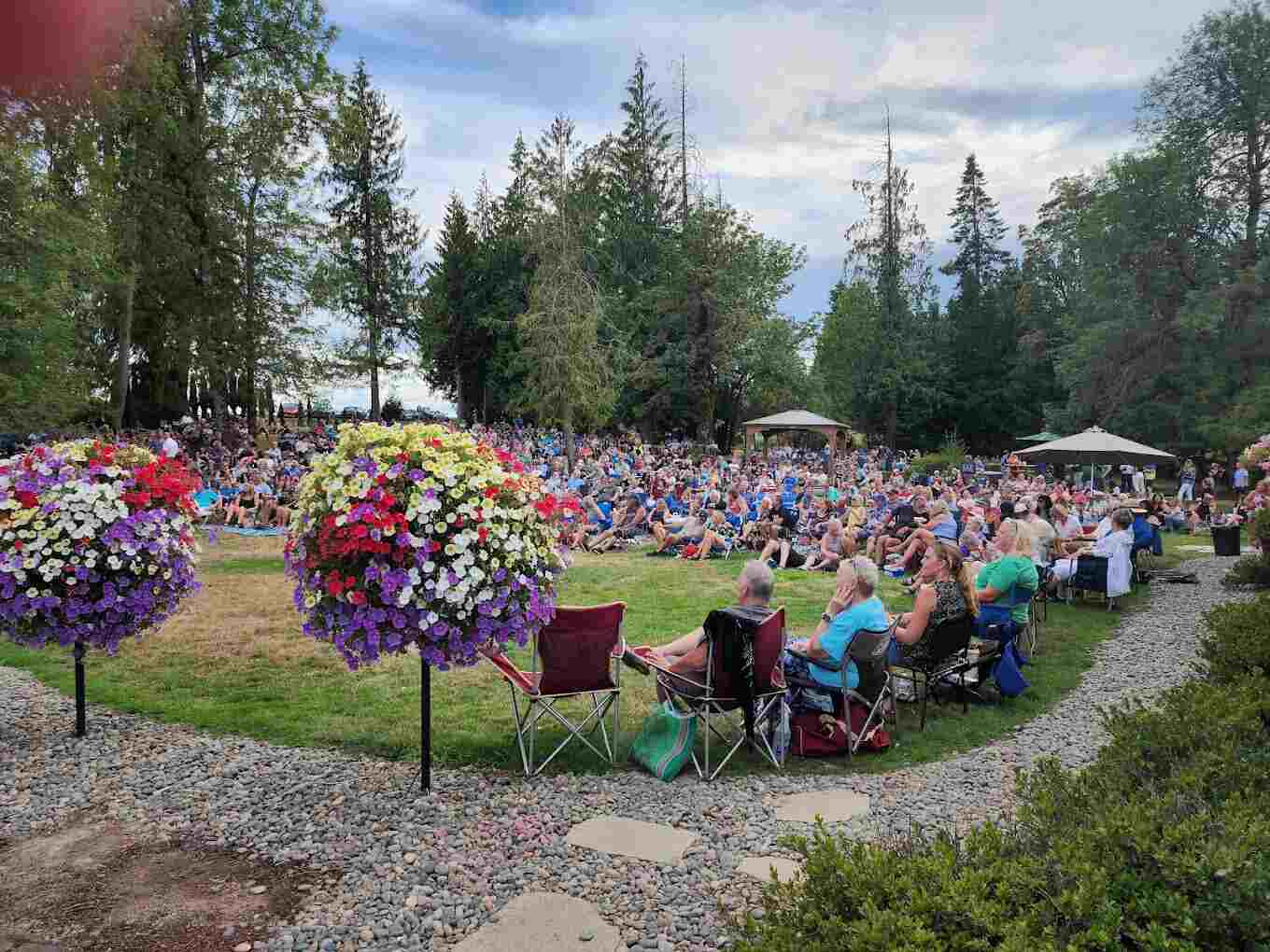 A crowd in lawn chairs watching an outdoor concert on the lawn at 14 Acres, hanging flower baskets on either side