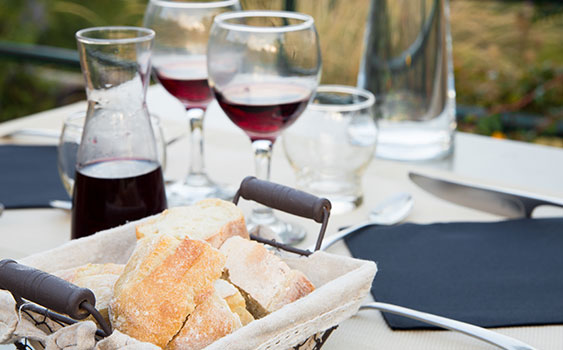 Two glasses of red wine and a carafe beside a basket of bread on an outdoor table at 14 Acres