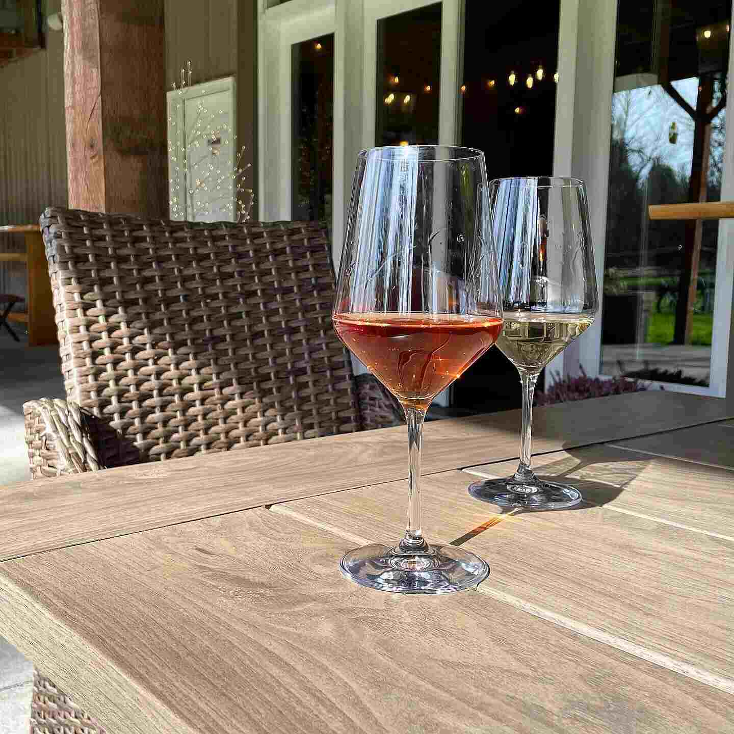 A glass of rosé and a glass of white wine on a wooden patio table outside the 14 Acres tasting room