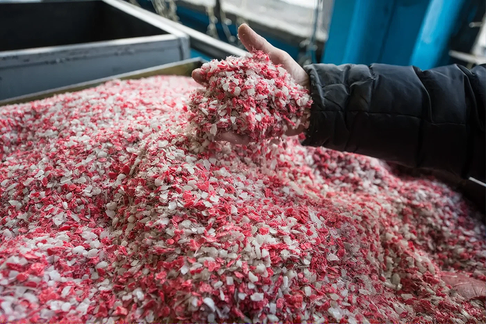 Hand holding a scoop of shredded red and white plastic flake recycling material