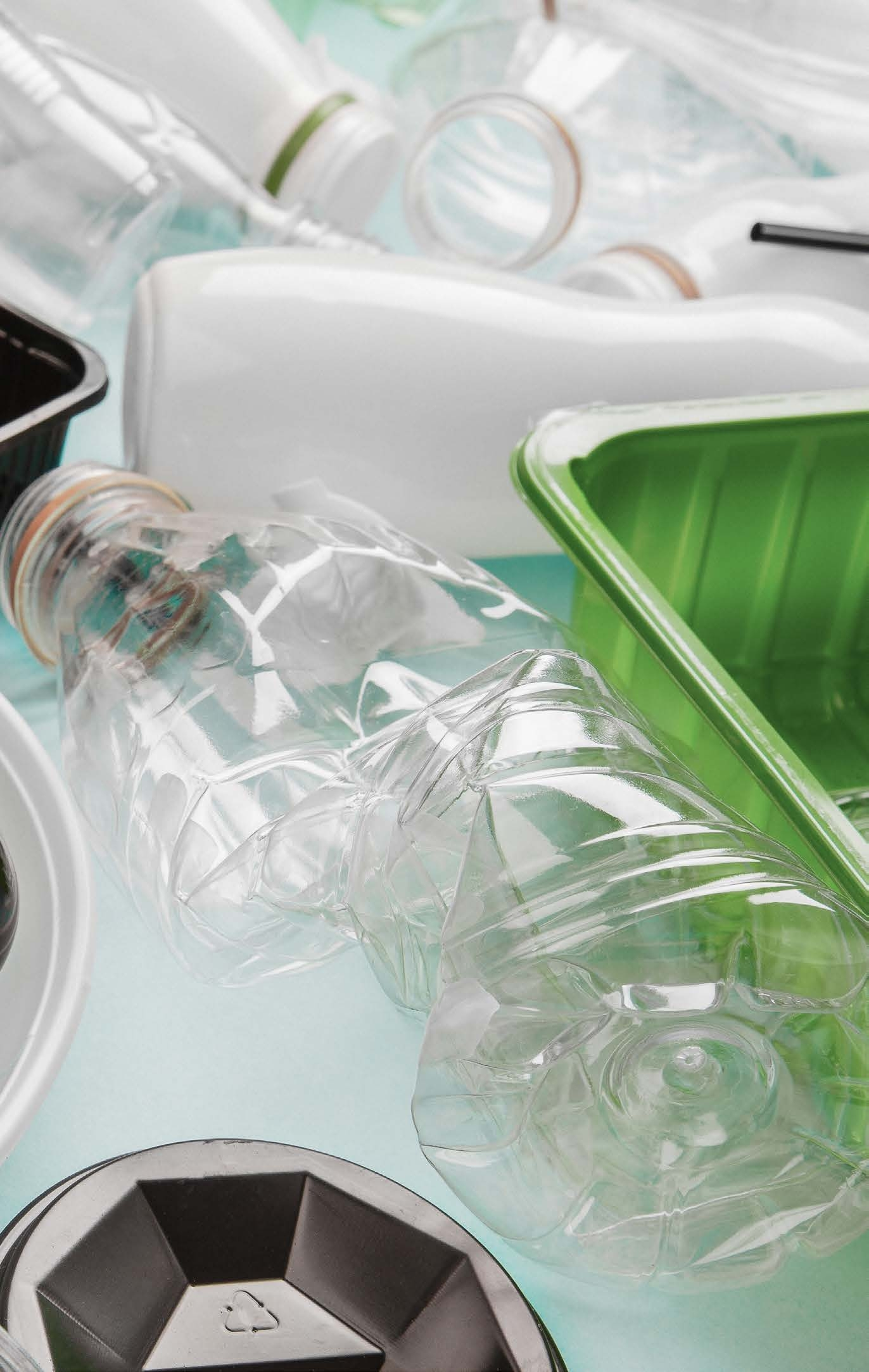 Close-up of mixed plastic packaging waste including bottles and a green tray for recycling