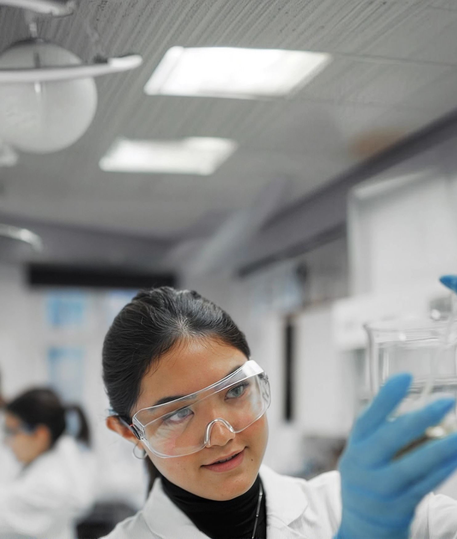 Scientist in safety goggles and blue gloves examining glassware in a research laboratory