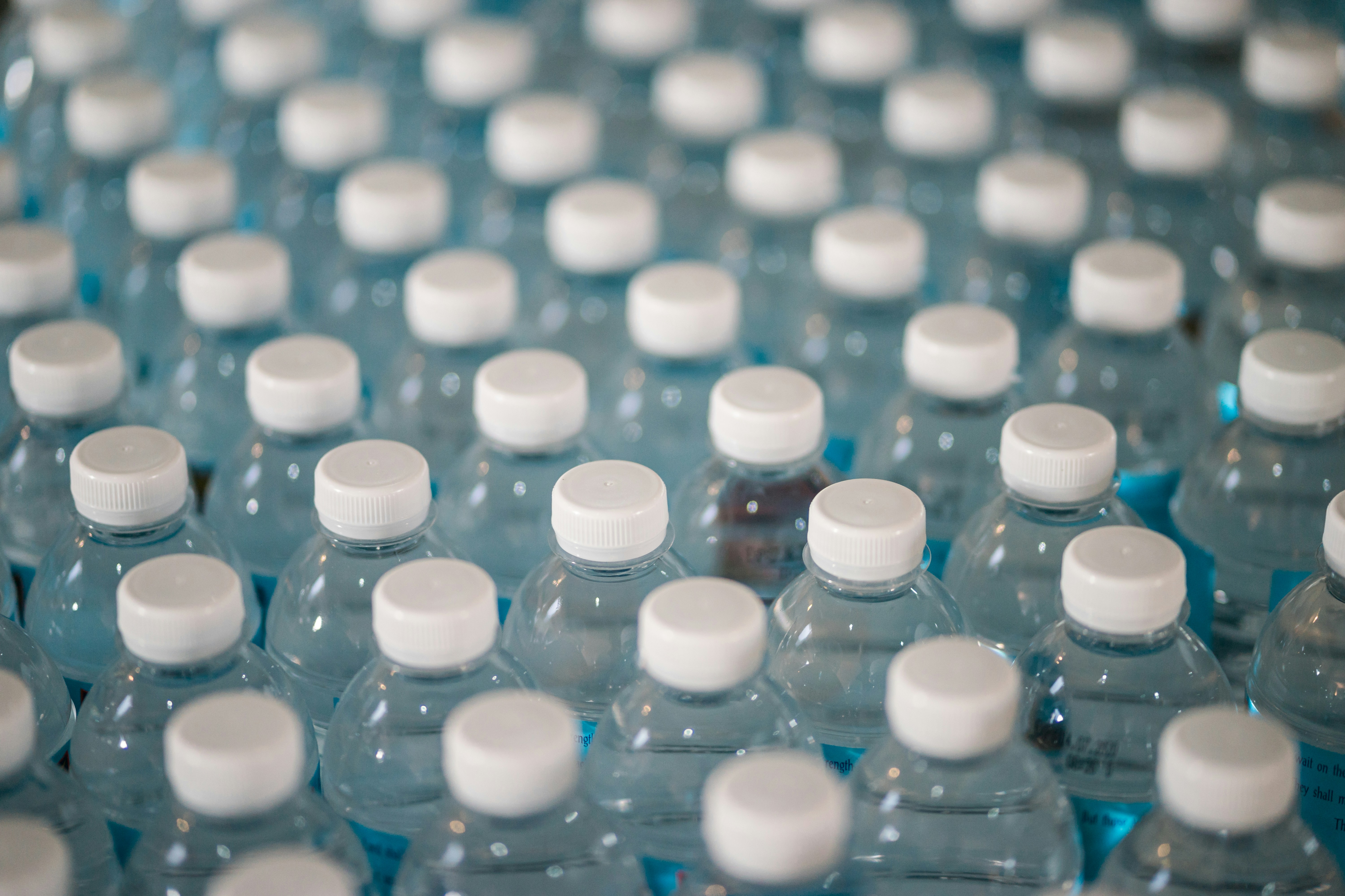 Rows of empty clear plastic water bottles with white caps ready for recycling