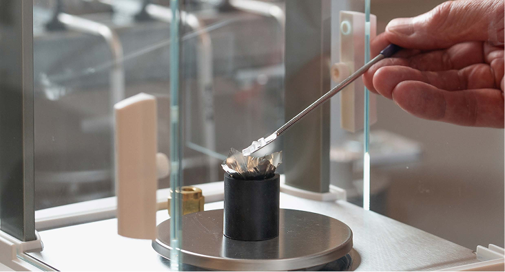 Lab technician using tweezers to place a plastic sample into a crucible on an analytical balance