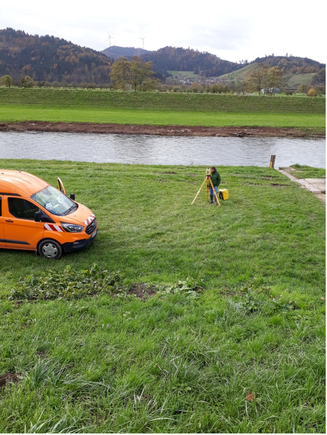 Vermessungsfahrzeug und Ingenieur mit Stativ am Gewässer
