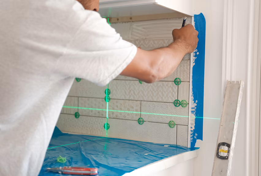 Flooring Services LLC installer setting tile backsplash using a laser level for precise alignment