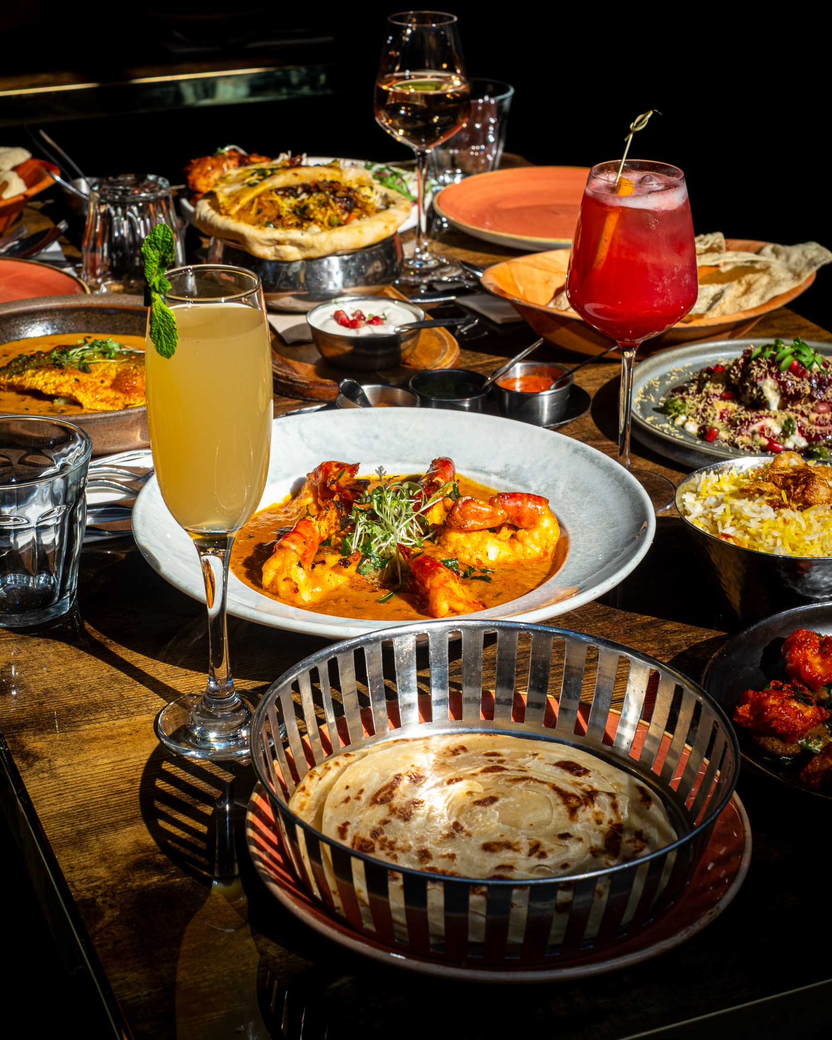 A vibrant Nutmeg dining table with Indian dishes, cocktails and naan