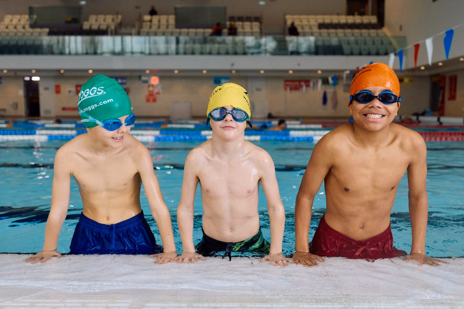 Three children smiling at the edge of the pool.