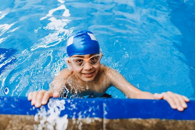 Boy sitting at the edge of the pool looking up smiling.