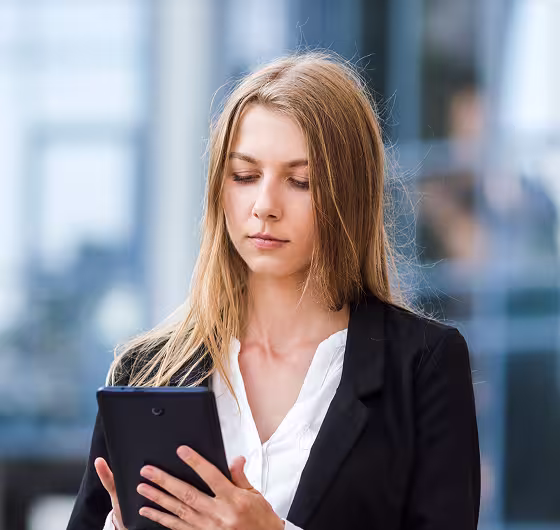 Professional woman with long blonde hair reading a tablet in an office setting.