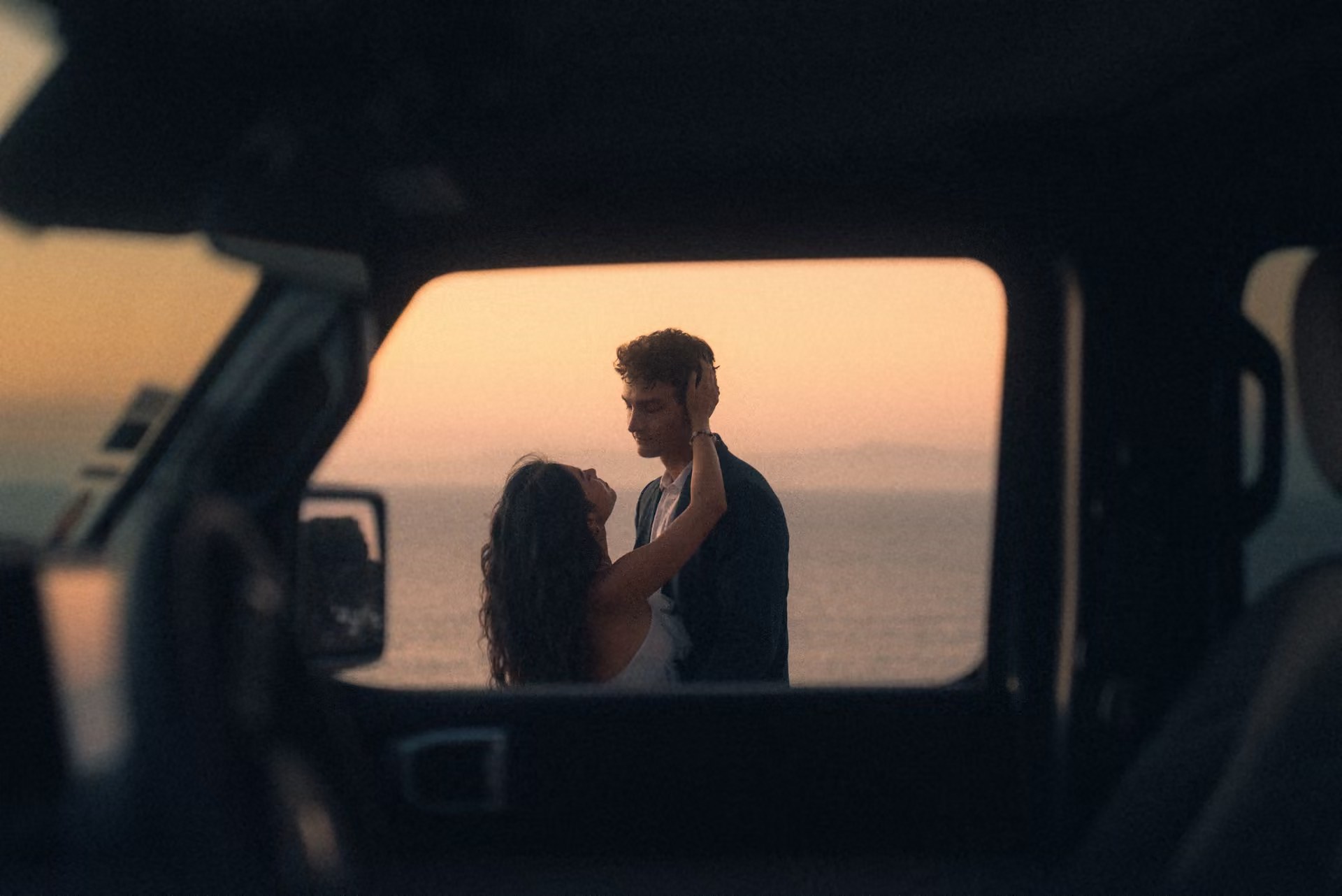 Bride and groom kissing in an arched window beneath a chandelier