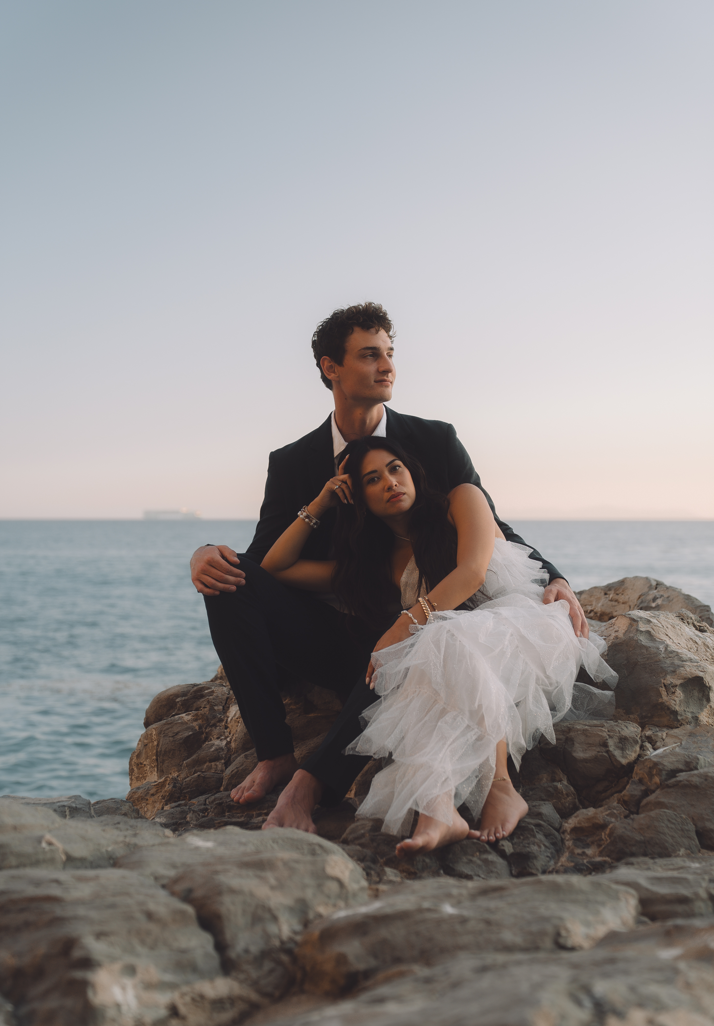 Couple sitting on seaside rocks at sunset