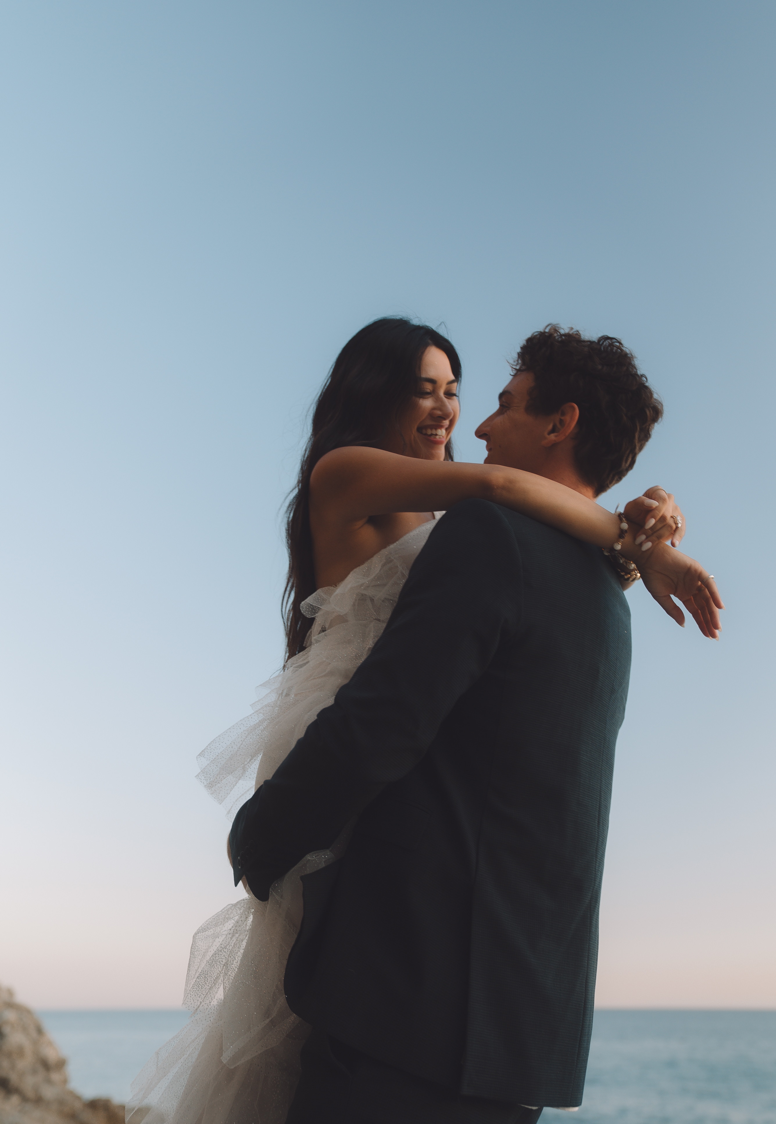 Groom lifting bride against a blue sky